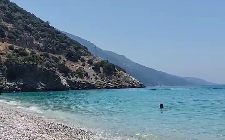 Turquoise sea and a white pebble beach below a steep green mountain near Fethiye.